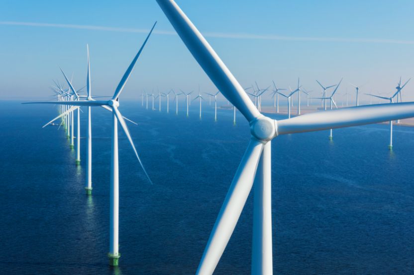 A row of wind turbines stands in the sea beneath a clear blue sky.
