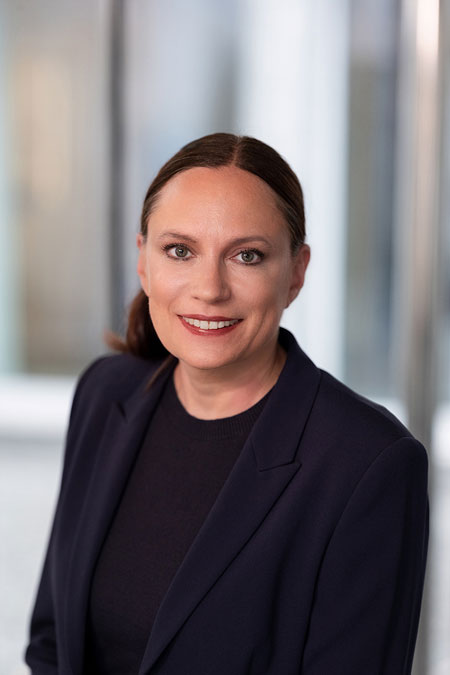 Dr Daniela B&uuml;chel, a member of the REWE Group&rsquo;s Executive Board responsible for Human Resources and Sustainability, is wearing a dark blazer and a black top against a blurred background.