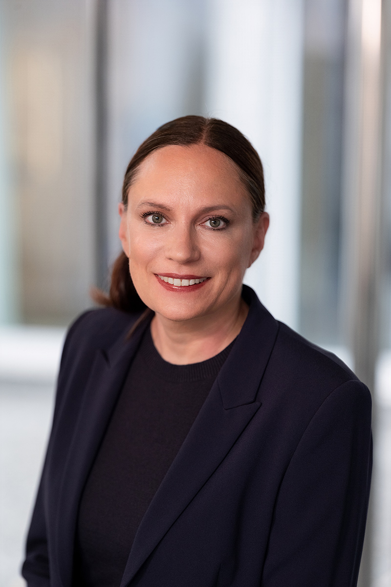 Dr Daniela B&uuml;chel, a member of the REWE Group&rsquo;s Executive Board responsible for Human Resources and Sustainability, is wearing a dark blazer and a black top against a blurred background.