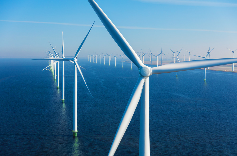 A row of wind turbines stands in the sea beneath a clear blue sky.